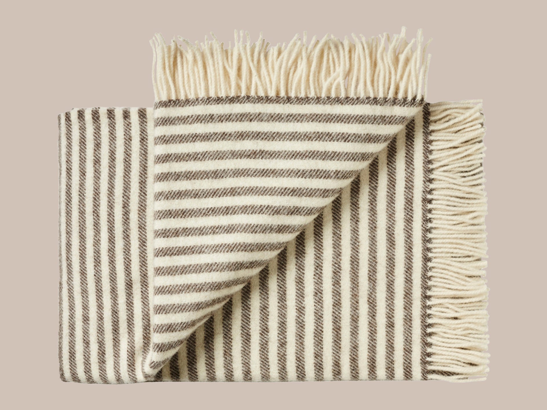 Uldplaid med frynser i skandinavisk uld i de smukkeste naturlige farver og mønstre. Et varmt bæredygtigt uldtæppe til dig , der elsker at varme dig med et tæppe.. Dette tæppe er i et smukt afstemt mønster i nougat farvet og lys beige. Mønstret er 50 cm stribet i hver ende og ensfarvet nougat i midten af tæppet. Frynserne er lys beige.